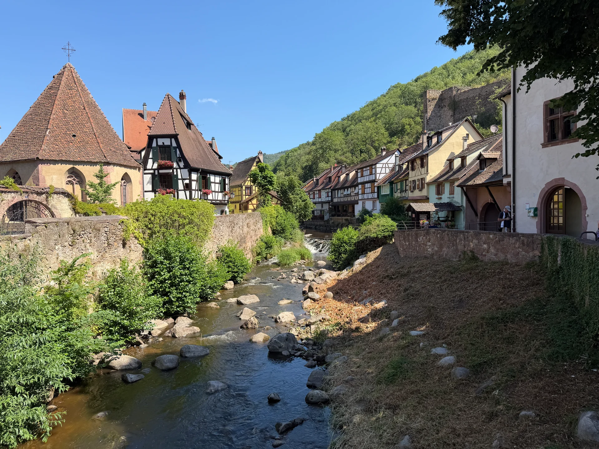 Timber-framed houses along the river in Kaysersberg with castle ruins on the hillside