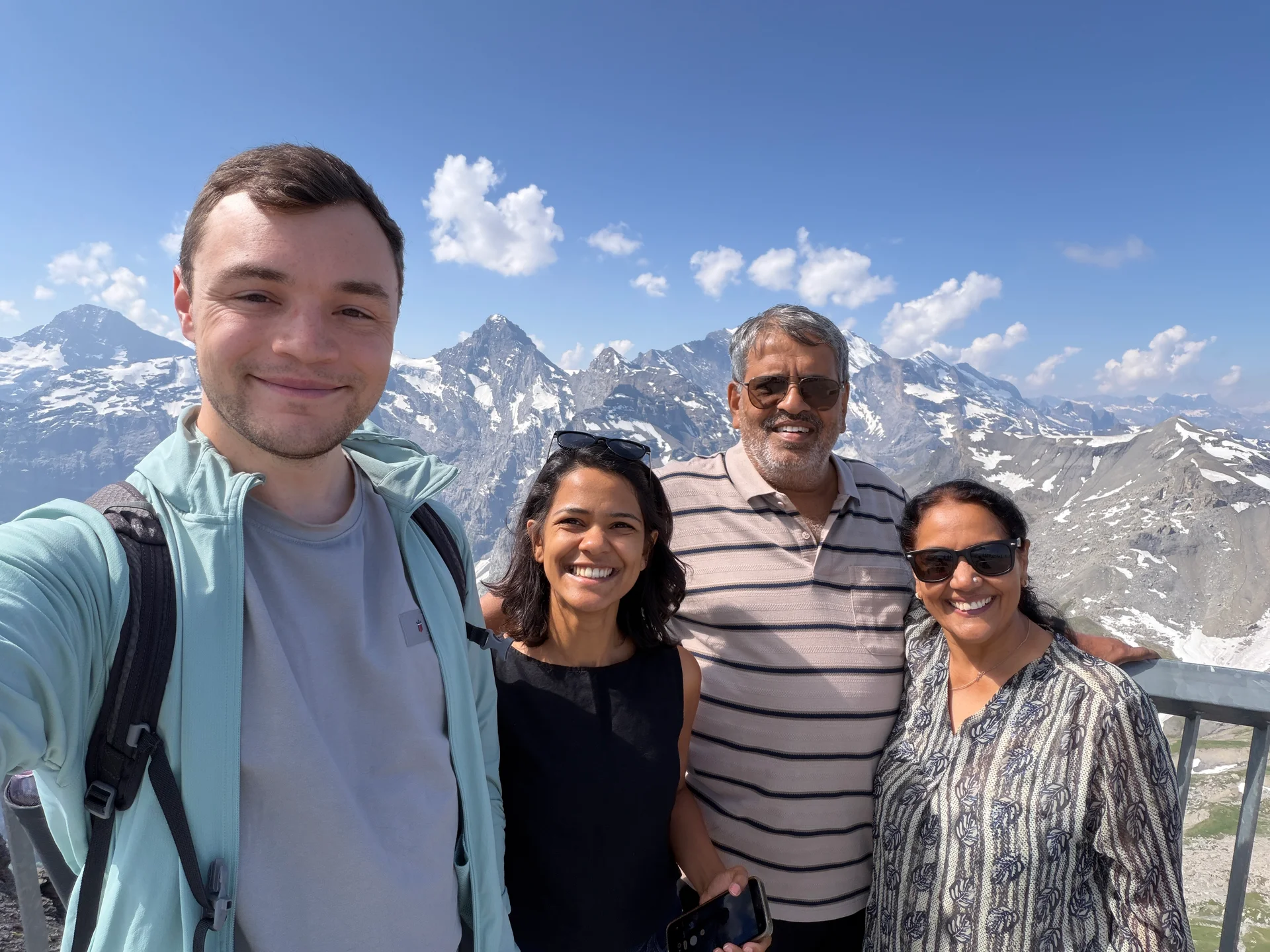 The whole group taking a selfie at a high Alpine viewpoint with snow-capped peaks behind